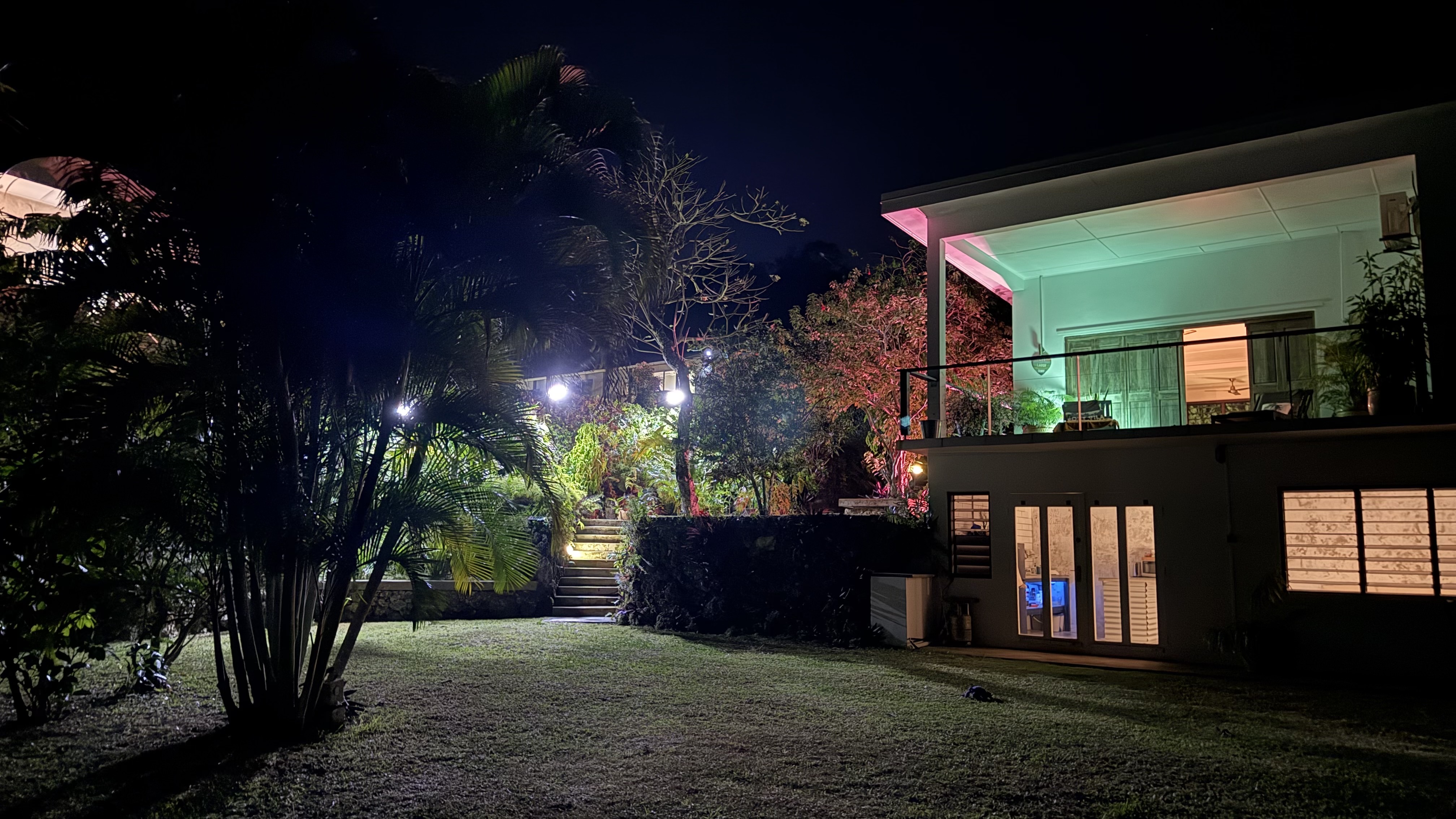 The two-storey house at night, warmly lit against a dark sky, with the family home upstairs and the apartment on the garden level below.