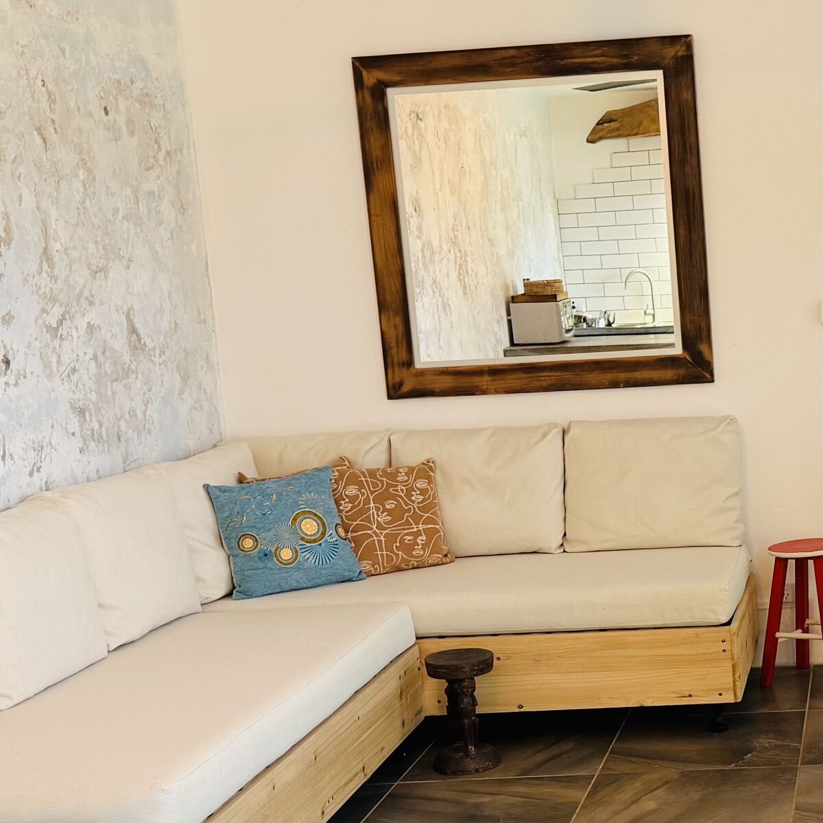 The lounge with a cream L-shaped sofa, a timber-framed mirror and a hallway with rainbow panelling leading through the apartment.